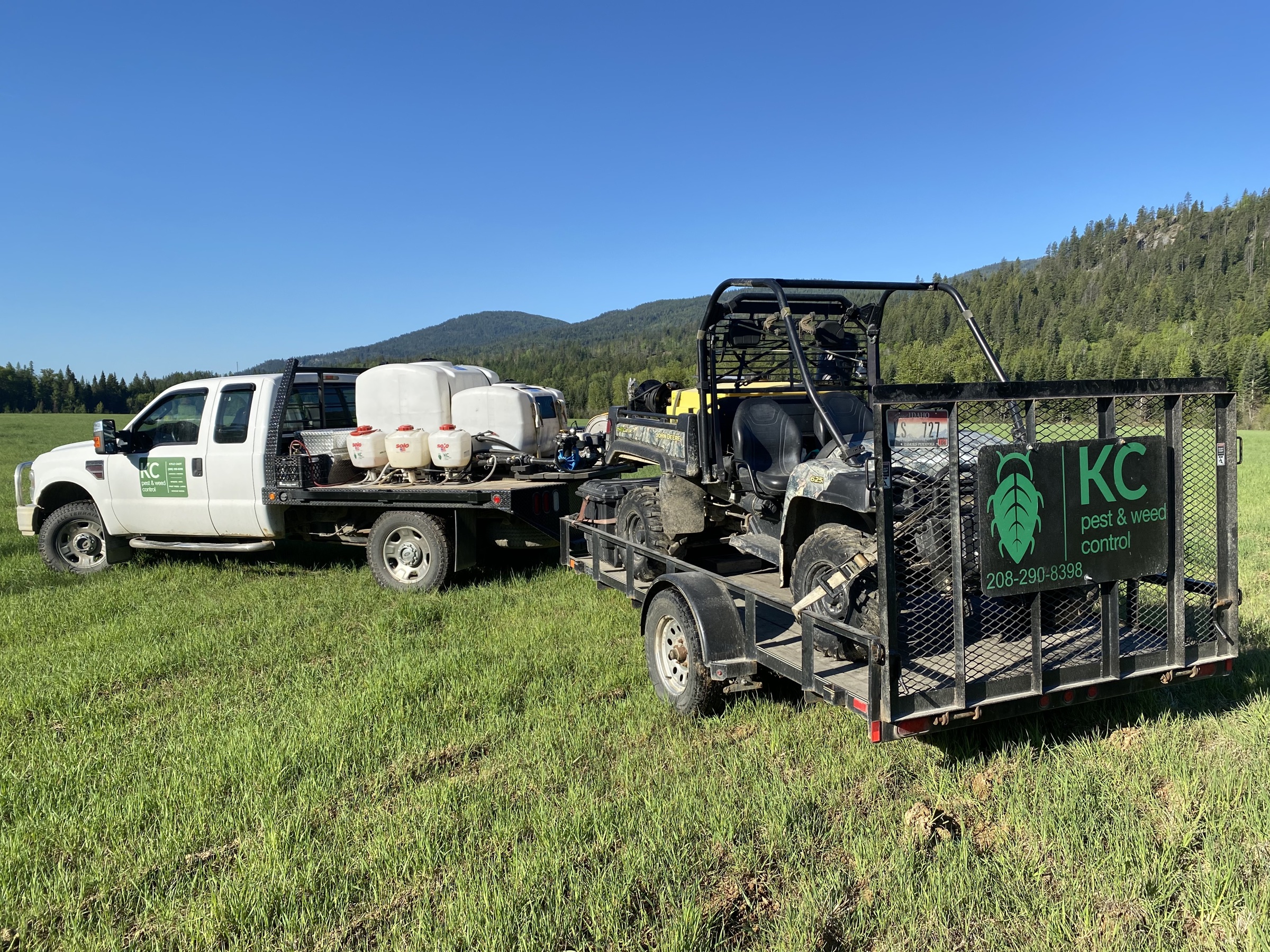 KC Pest and Weed spraying truck, tanks, ATV, and trailer in a rural pasture